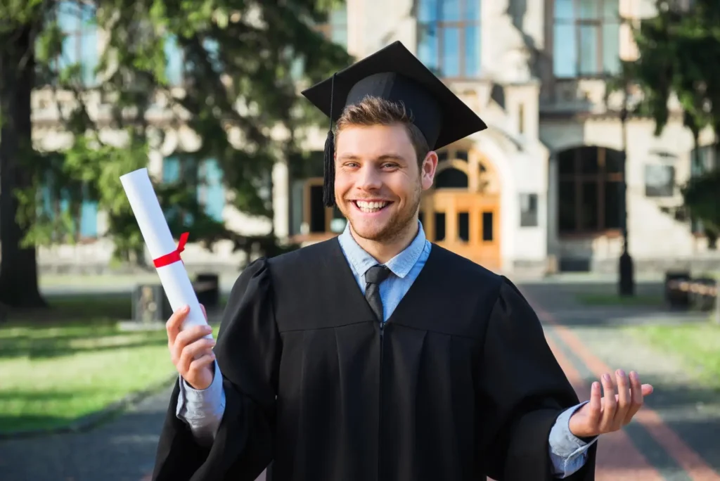 Happy graduate holding diploma in front of university building.